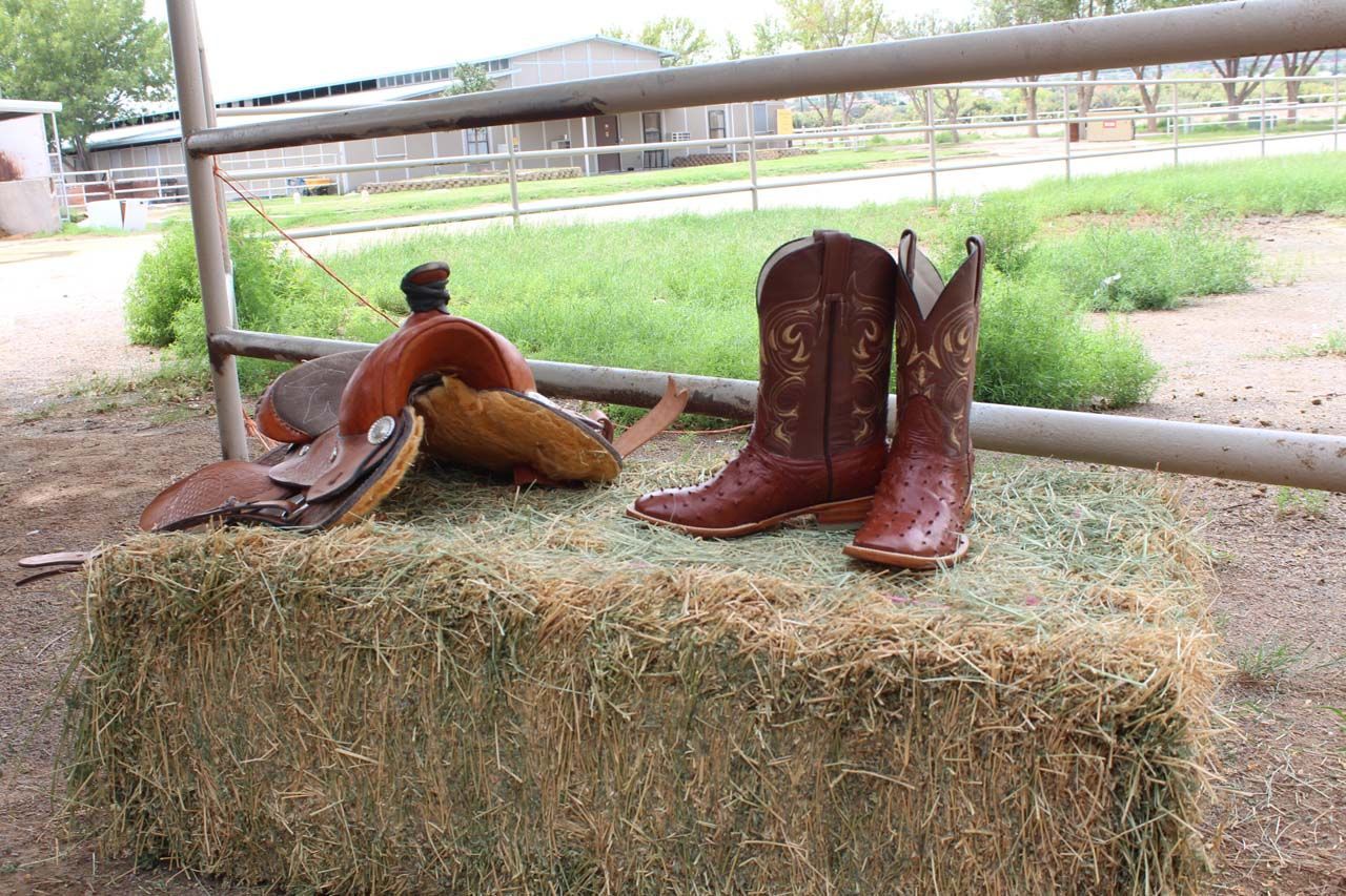A pair of cowboy boots and a saddle on a bale of hay