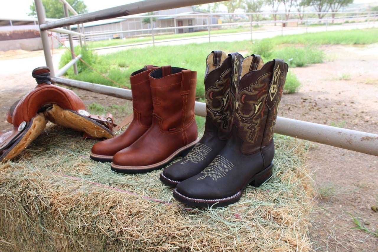 Two pairs of cowboy boots are sitting on top of a bale of hay.