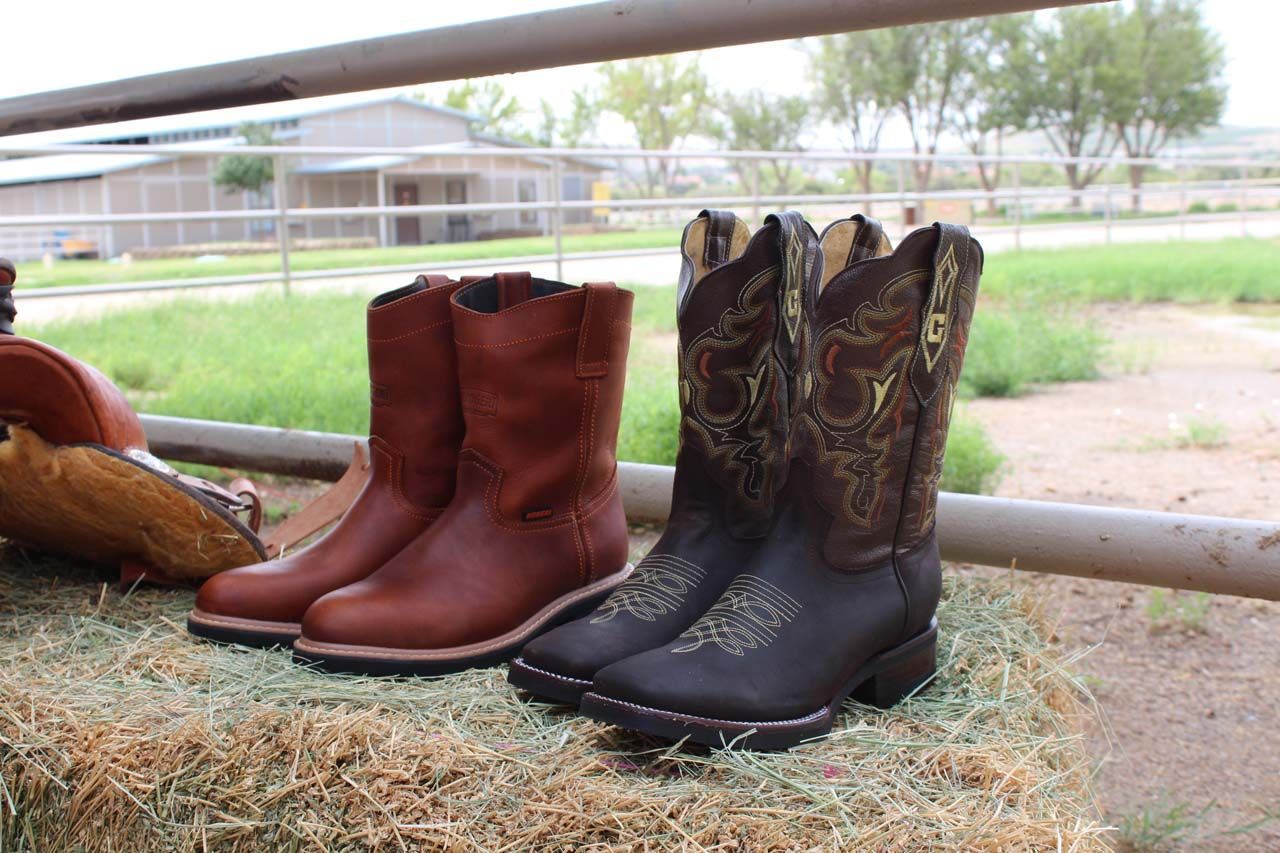 Two pairs of cowboy boots are sitting on top of a bale of hay.