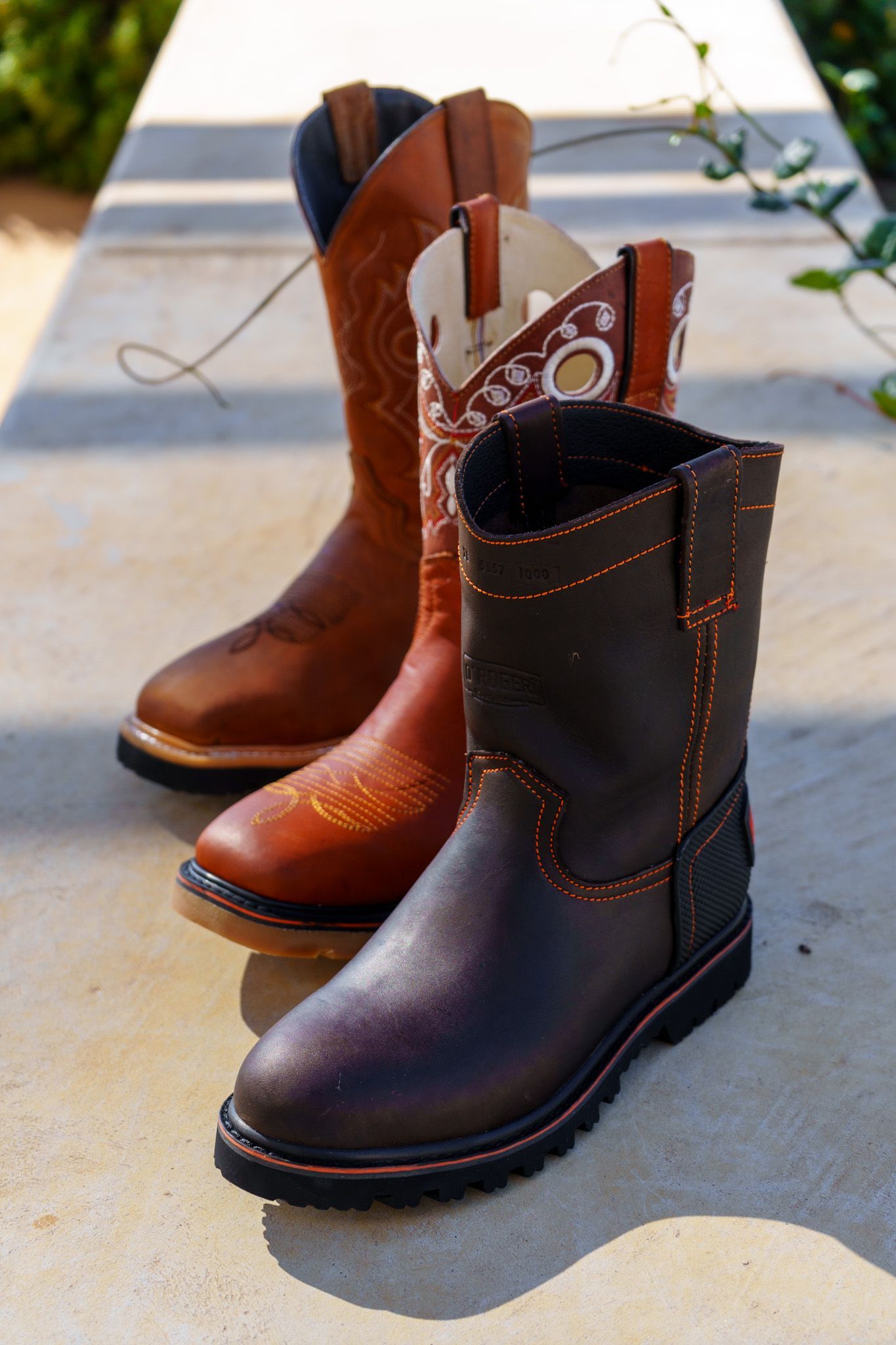 Three pairs of cowboy boots are sitting on a sidewalk.