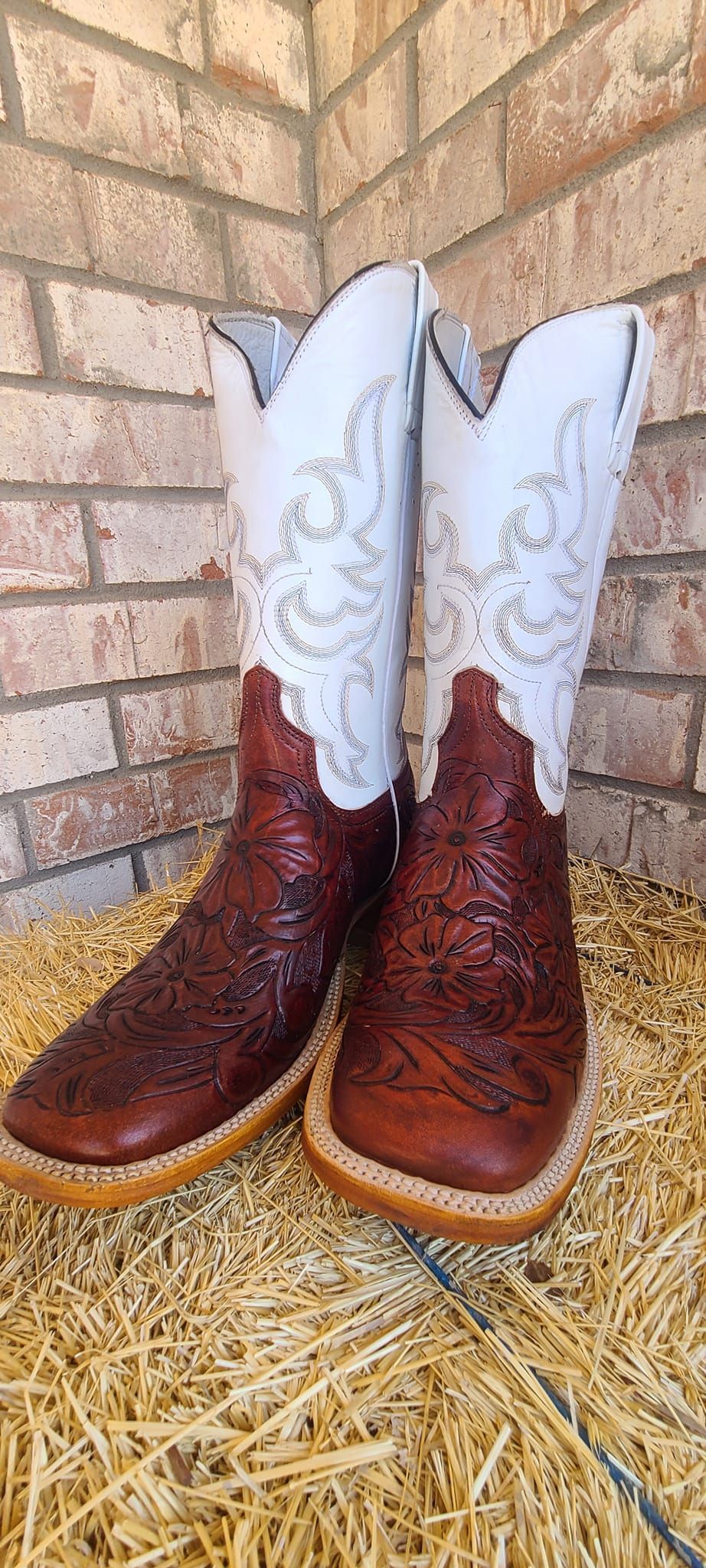 A pair of brown and white cowboy boots are sitting on a pile of hay.