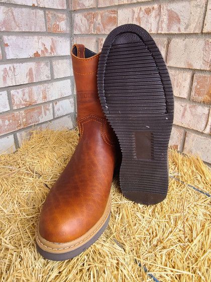 A pair of brown leather boots are sitting on top of a pile of hay.
