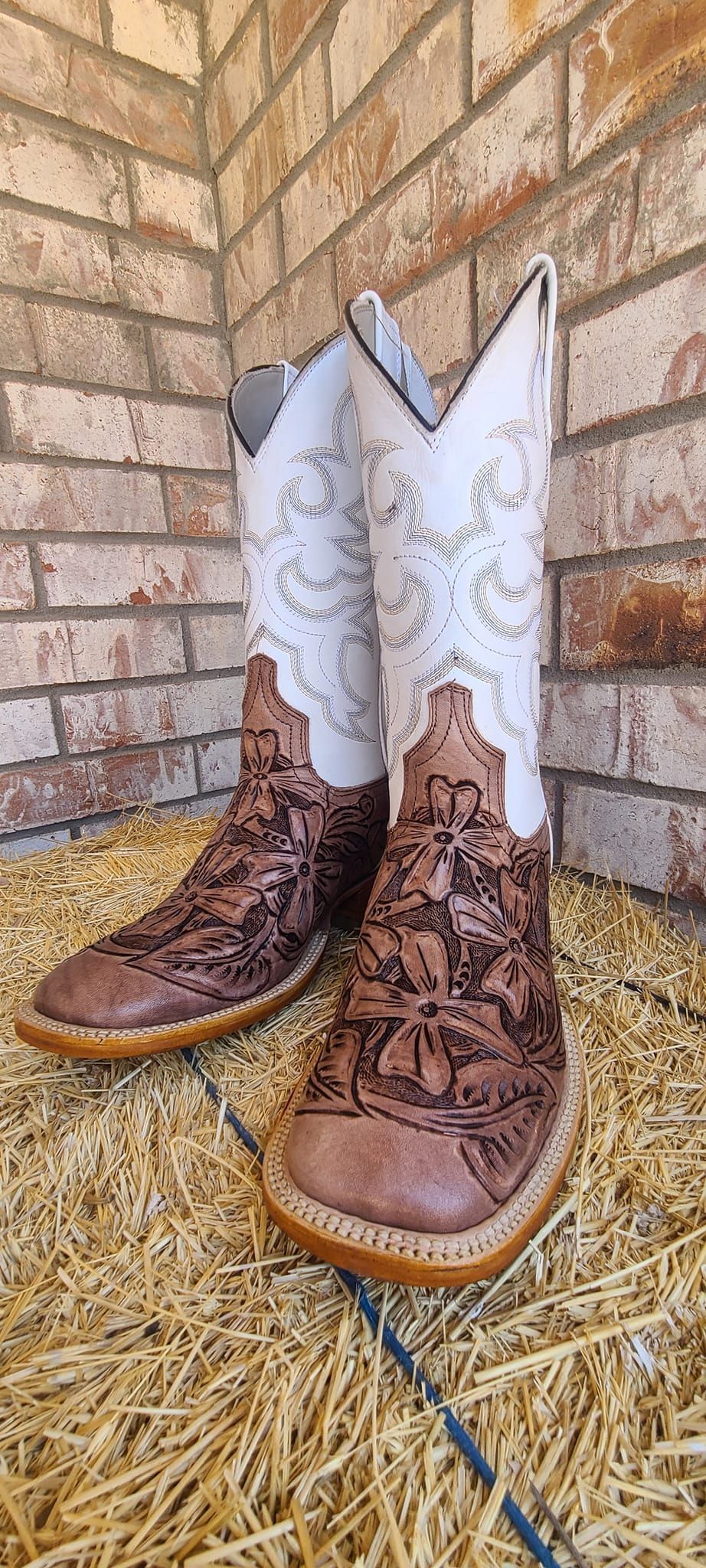 A pair of brown and white cowboy boots are sitting on a pile of hay.