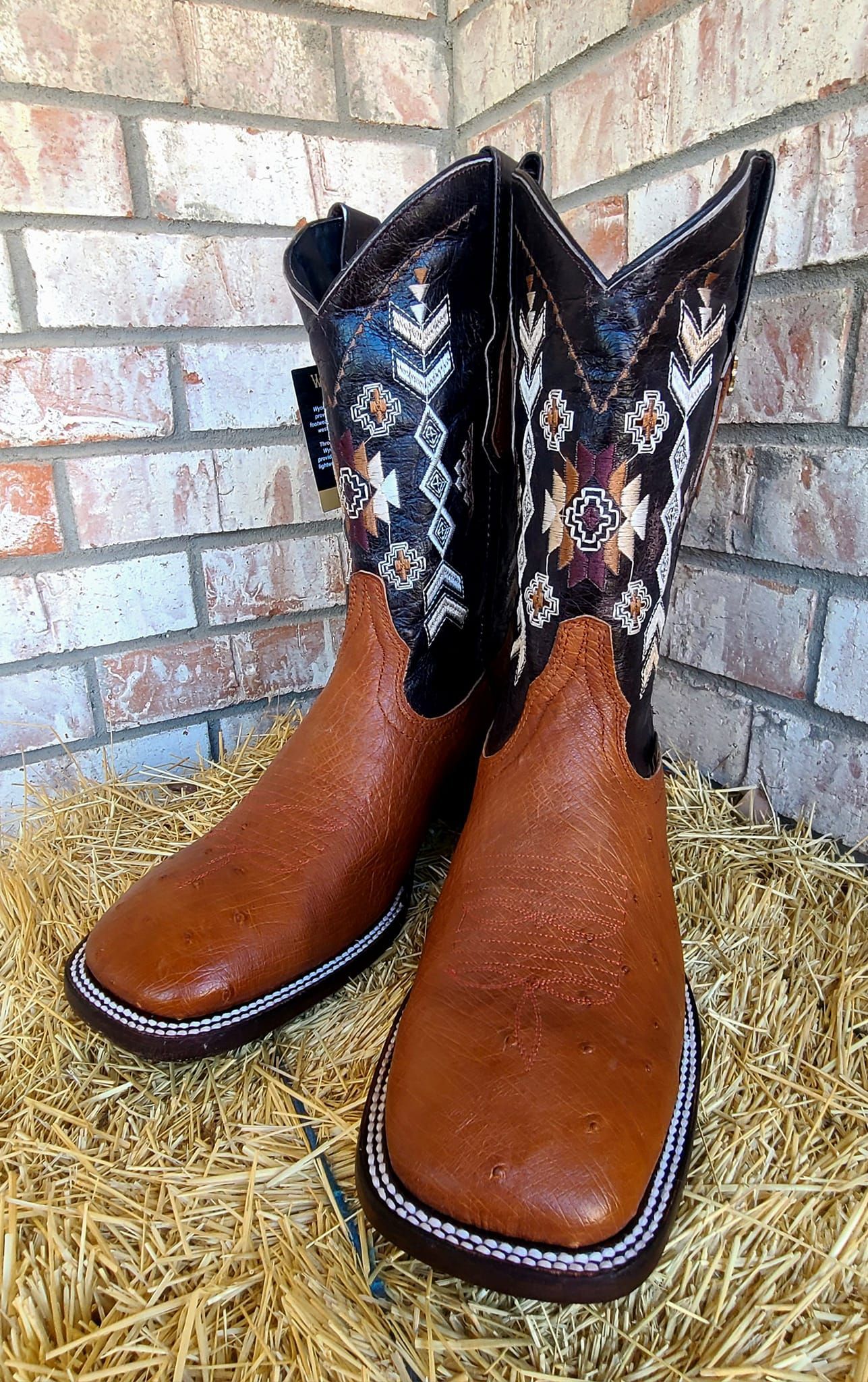 A pair of brown cowboy boots are sitting on top of a pile of hay.