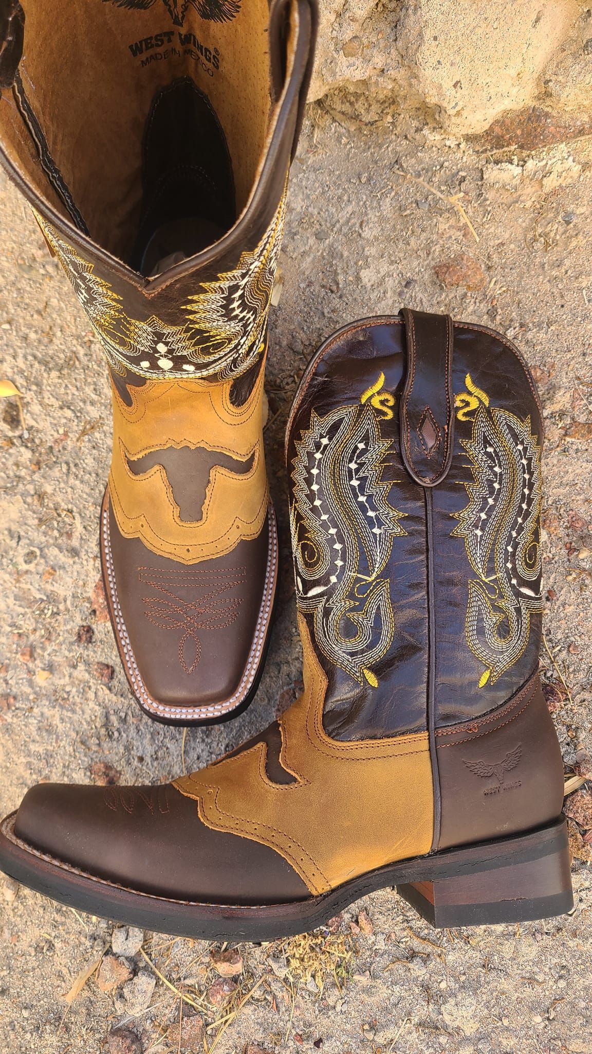 A pair of brown and yellow cowboy boots are sitting on the ground.