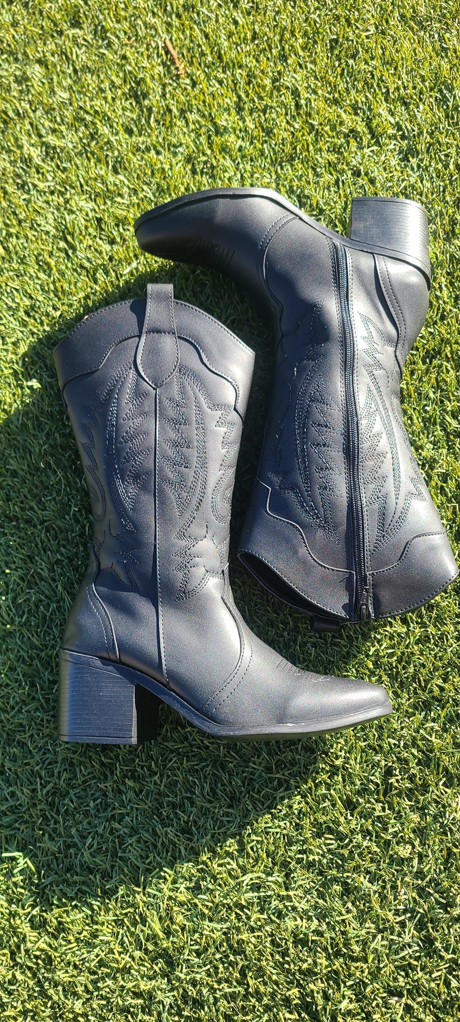 A pair of black cowboy boots are sitting on top of a lush green field.