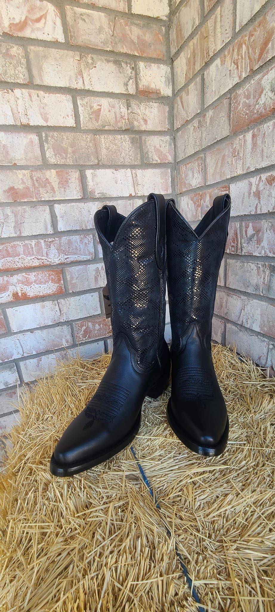 A pair of black cowboy boots are sitting on top of a pile of hay.