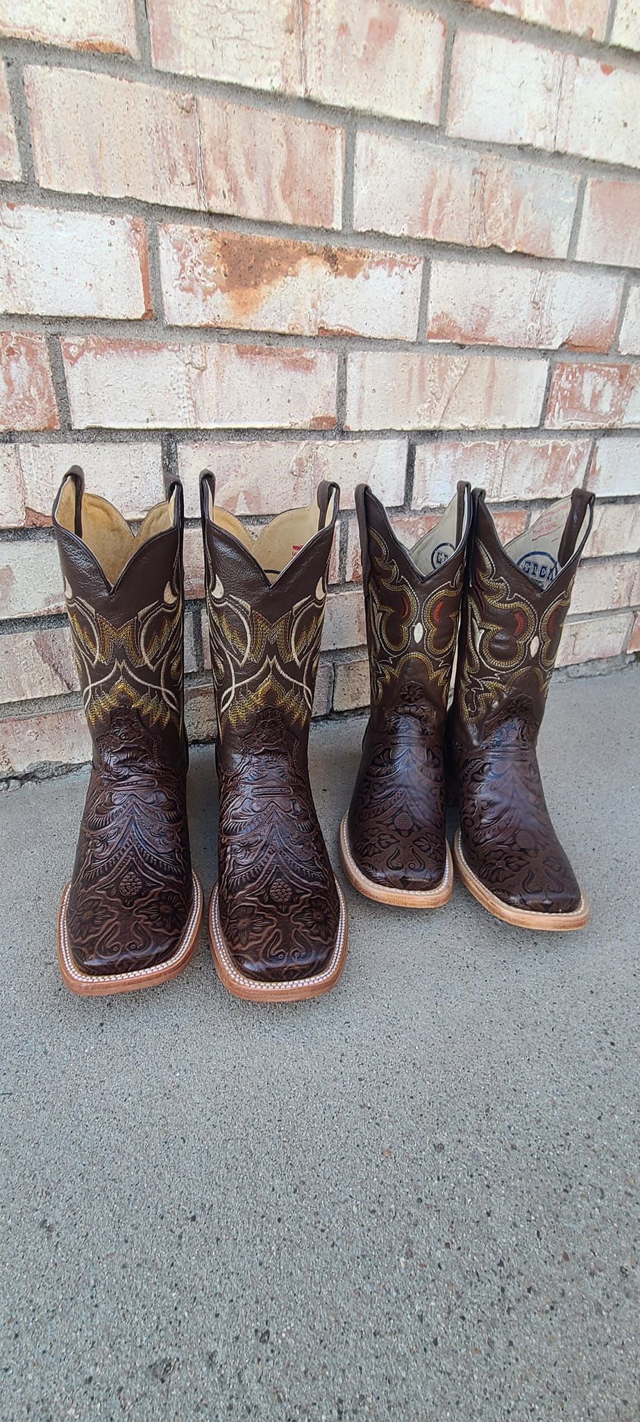 Three pairs of cowboy boots are sitting on the ground in front of a brick wall.