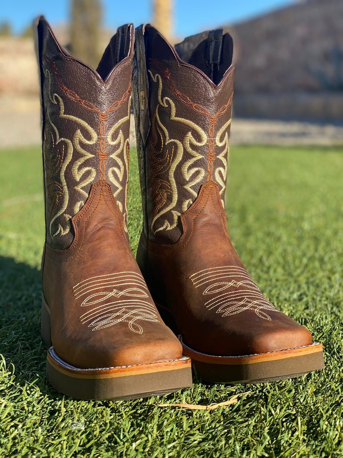 A pair of brown cowboy boots are sitting on top of a lush green field.