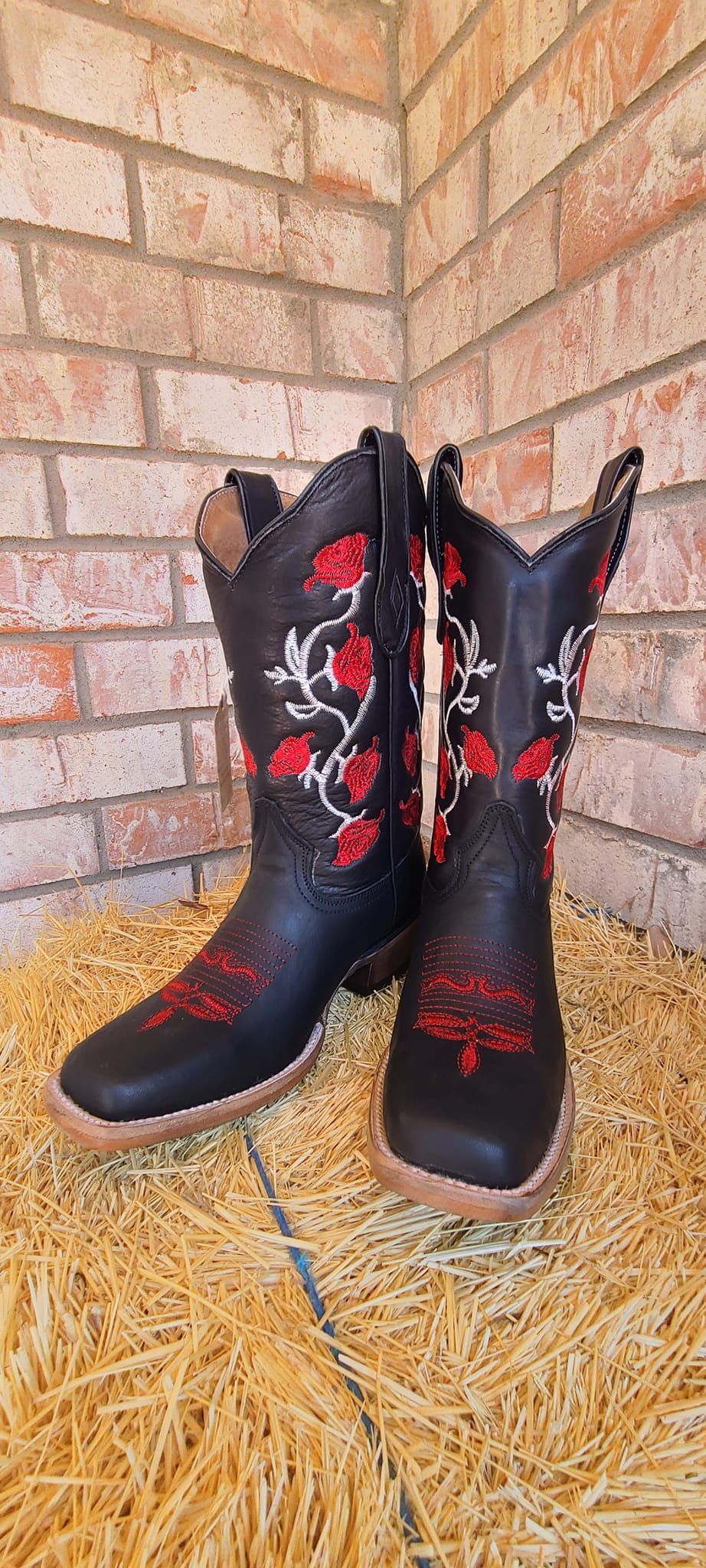 A pair of black and red cowboy boots are sitting on a pile of hay.