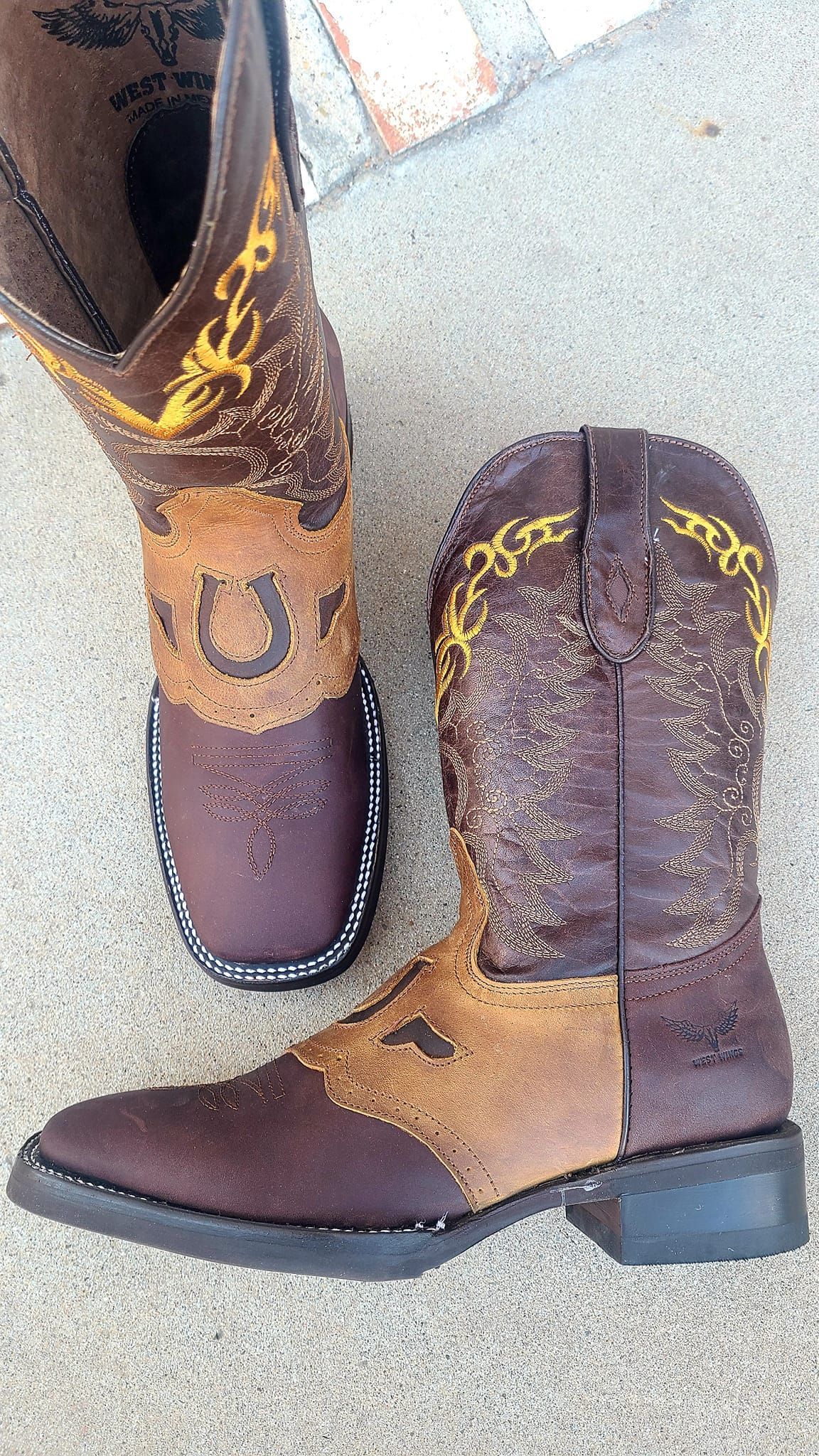 A pair of brown and tan cowboy boots are sitting on a concrete surface.