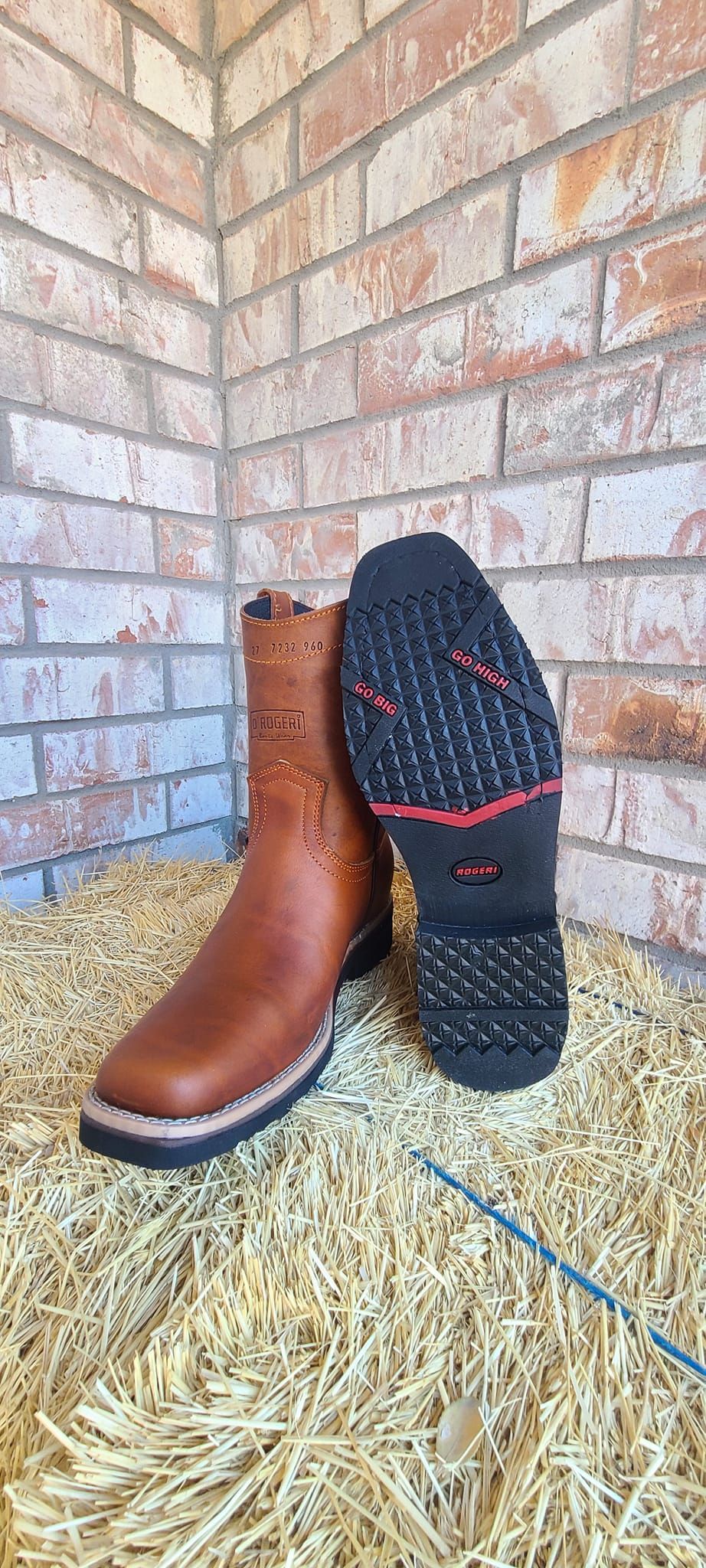 A pair of brown cowboy boots are sitting on top of a pile of hay.