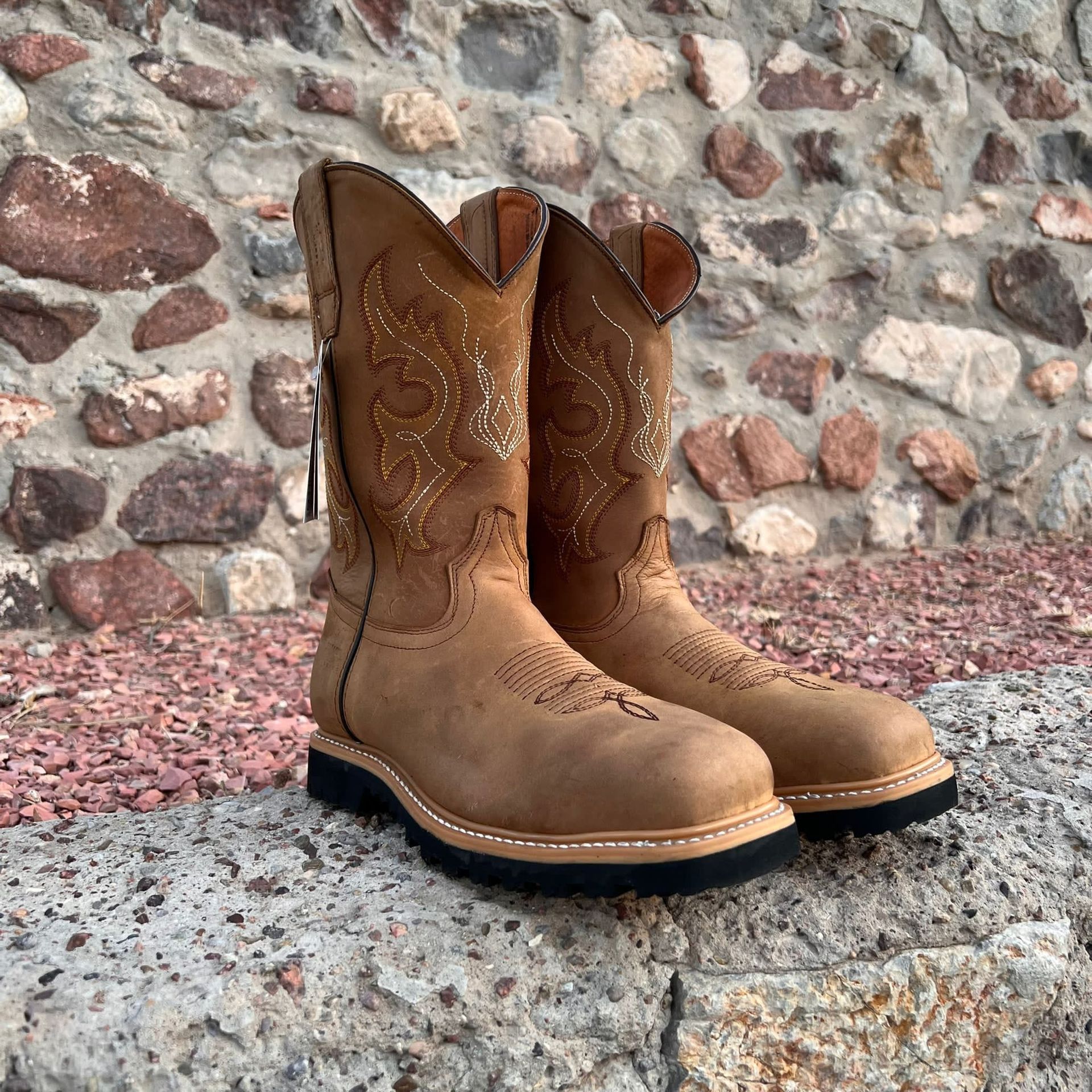 A pair of brown cowboy boots are sitting on a rock in front of a stone wall.