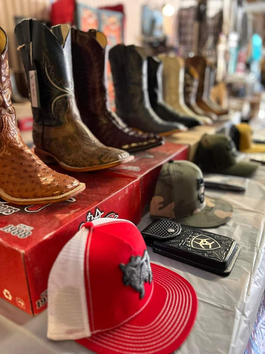 A row of cowboy boots , hats , wallets and cell phones on a table.