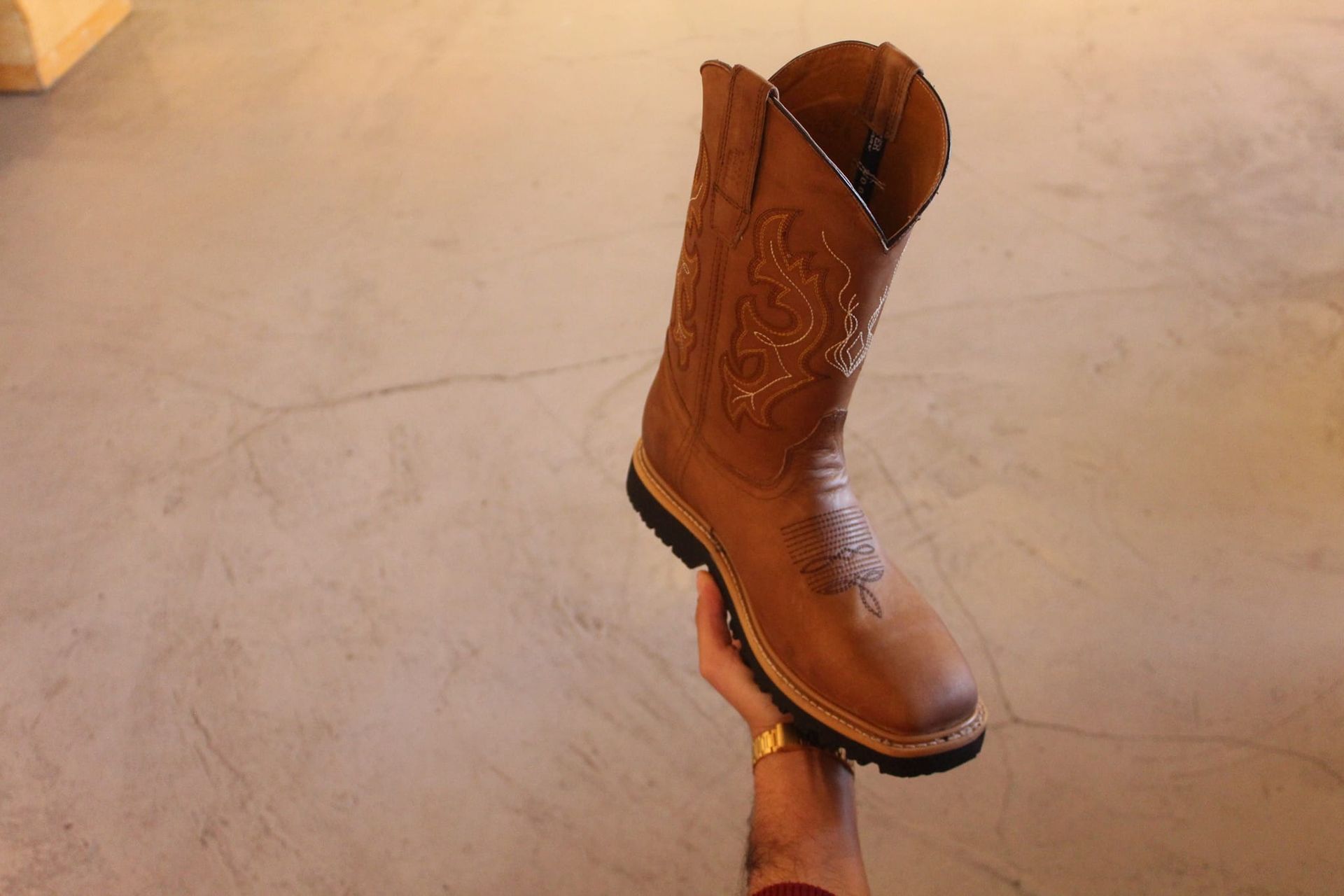 A person is holding a pair of brown cowboy boots in their hand.