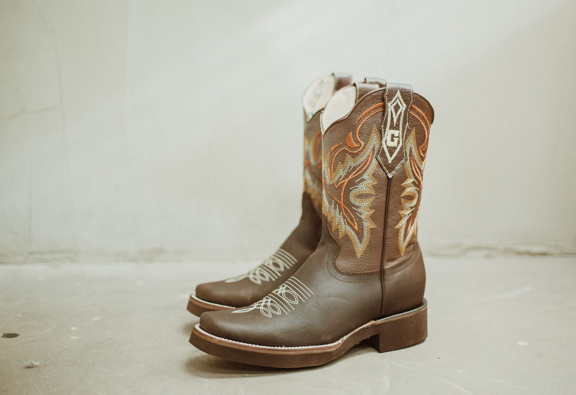 A pair of brown cowboy boots are sitting on a white surface.