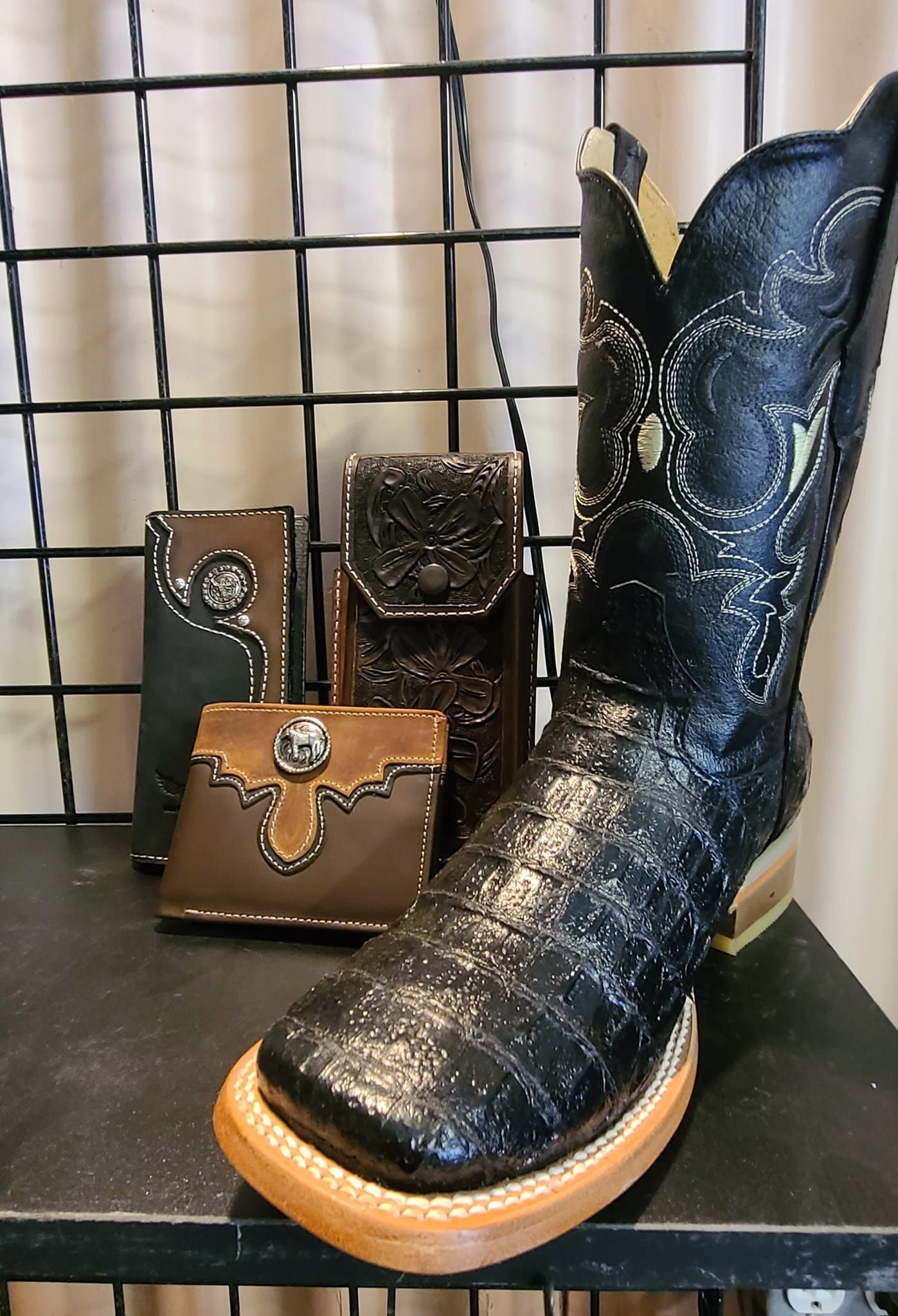 A pair of black cowboy boots are sitting on a shelf next to a wallet.