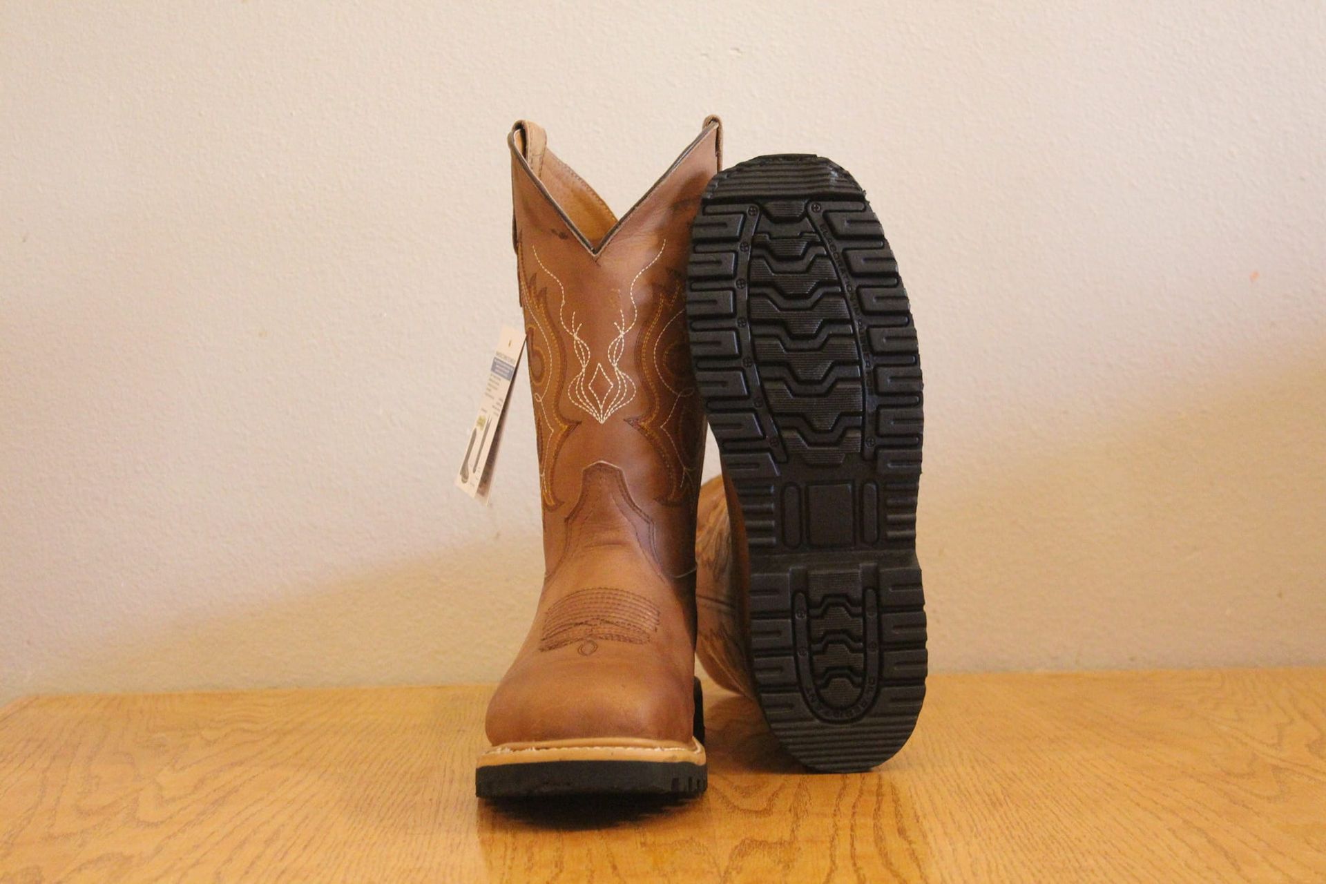 A pair of brown cowboy boots are sitting on a wooden table.