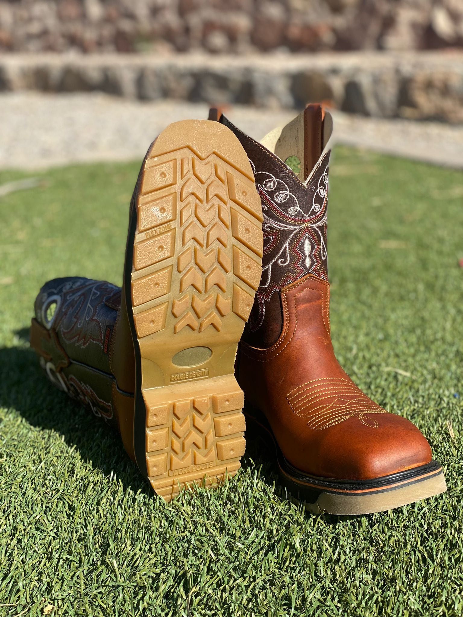 A pair of brown cowboy boots are sitting on top of a lush green field.