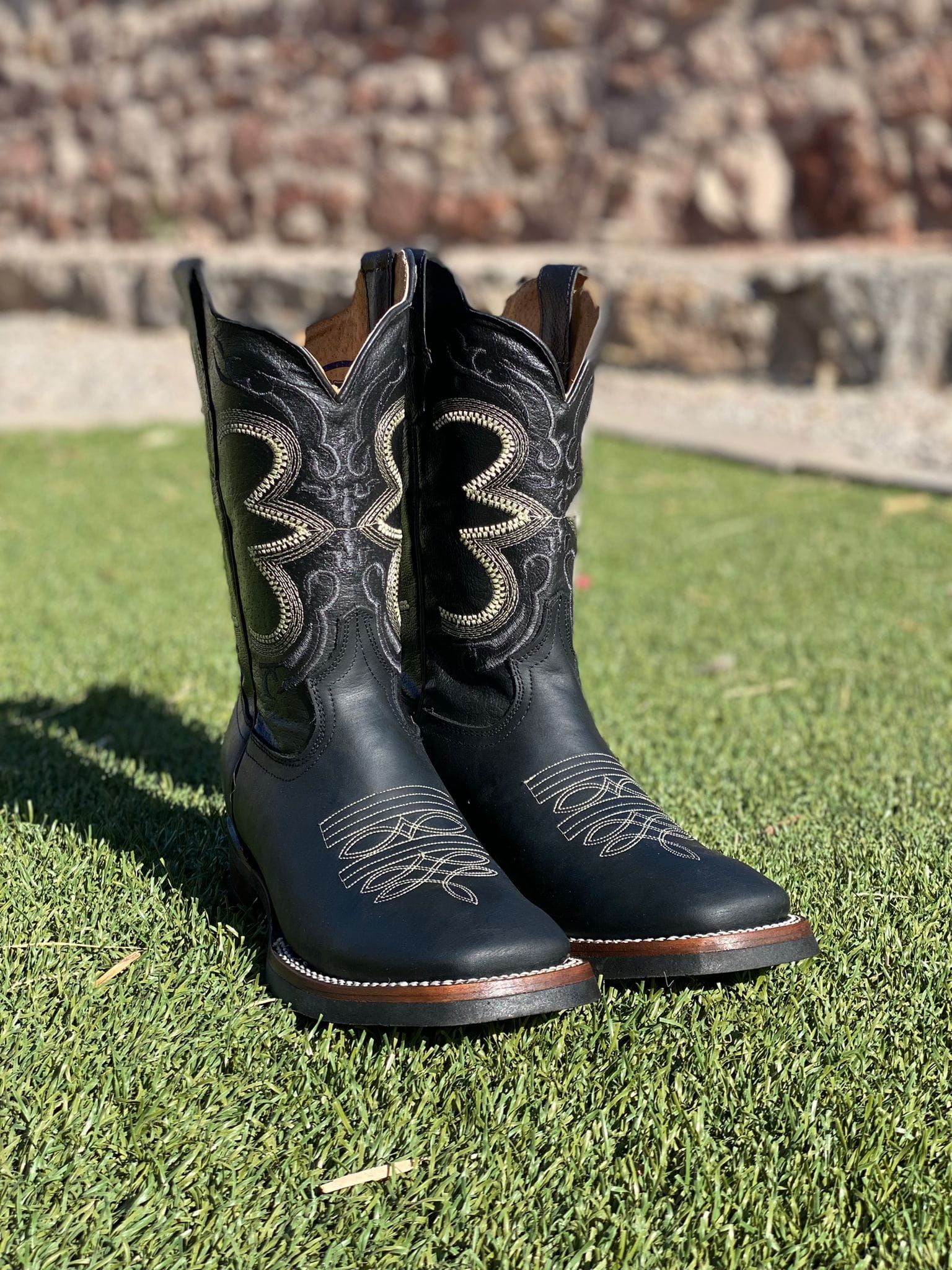 A pair of black cowboy boots are sitting on top of a lush green field.