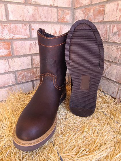 A pair of brown boots are sitting on a pile of hay in front of a brick wall.