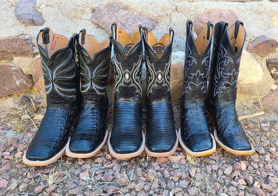 A row of black cowboy boots are lined up in front of a stone wall.