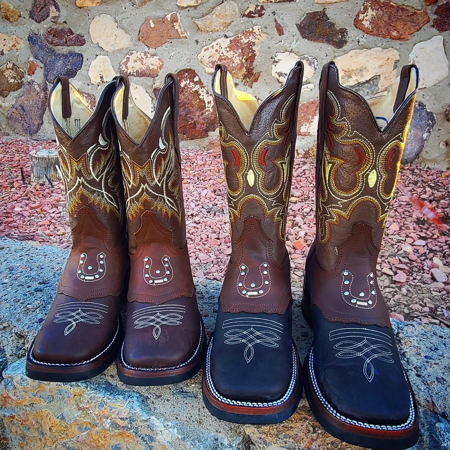 Three pairs of cowboy boots are sitting on a rock in front of a stone wall.