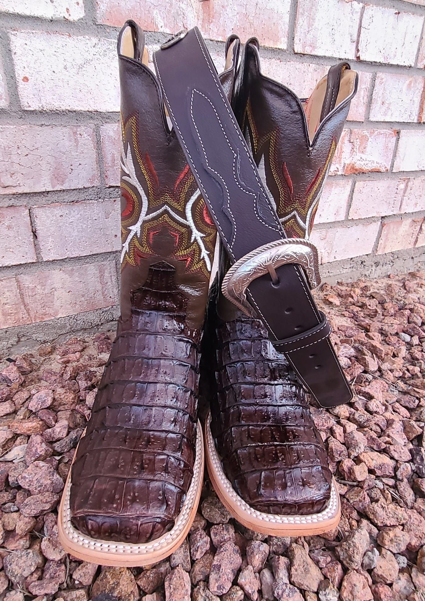 A pair of brown cowboy boots and a brown belt are sitting on a pile of rocks.