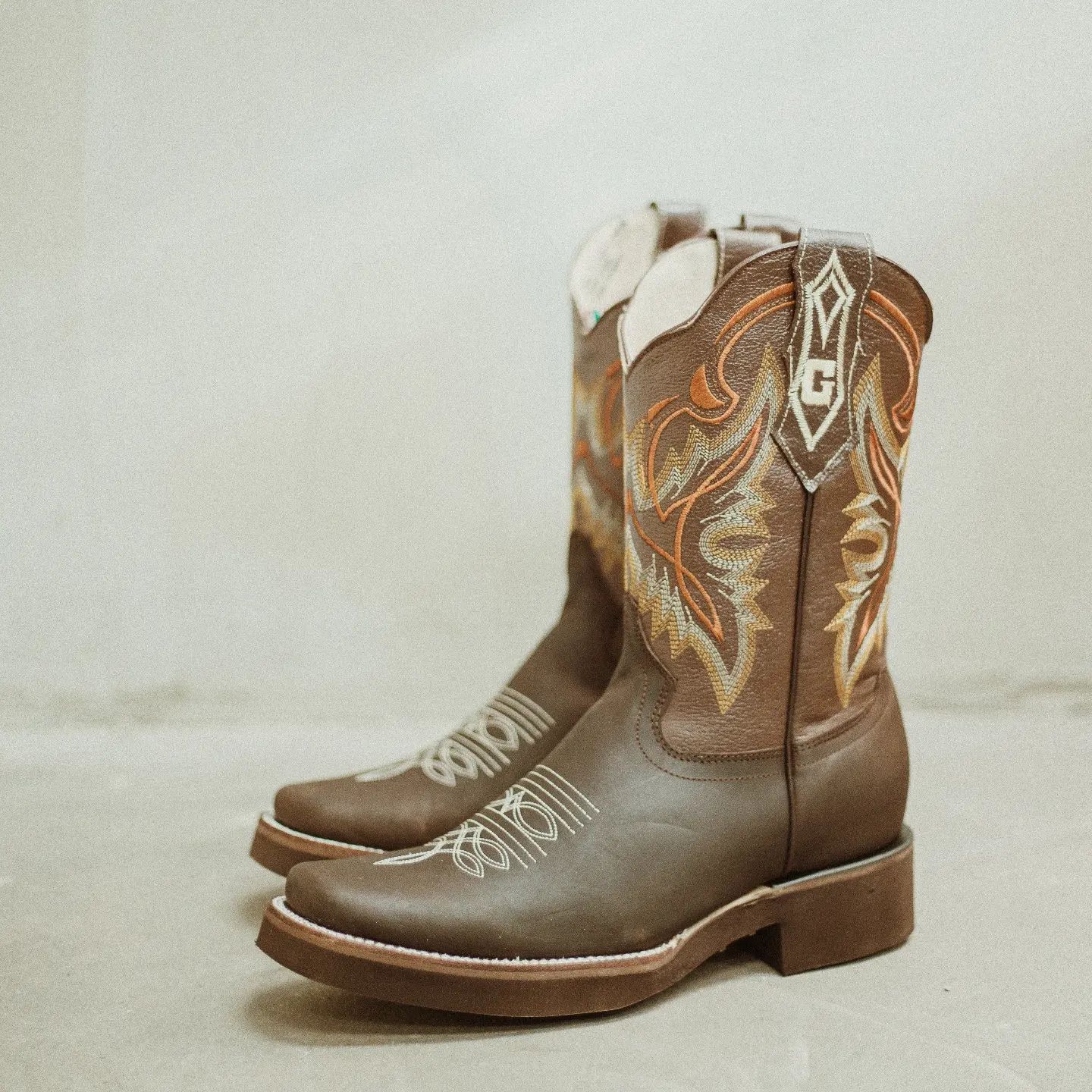 A pair of brown cowboy boots with the letter g on the side