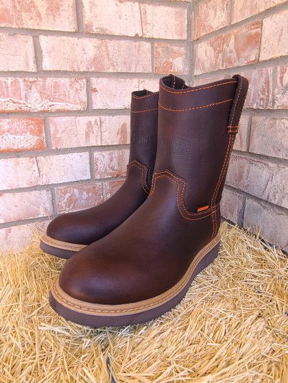 A pair of brown boots are sitting on a pile of hay in front of a brick wall.