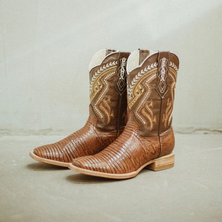 A pair of brown cowboy boots are sitting on a concrete surface.