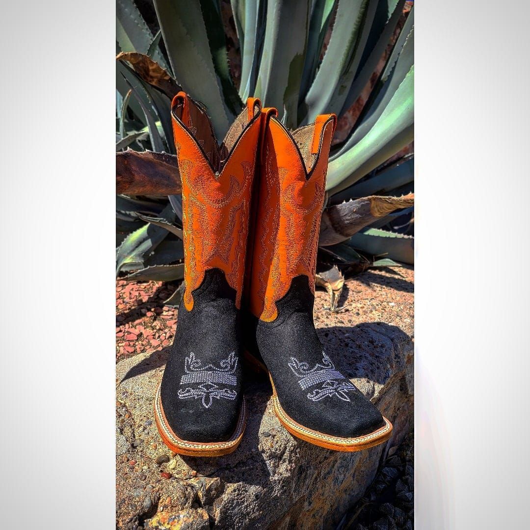 A pair of black and orange cowboy boots are sitting on a rock.