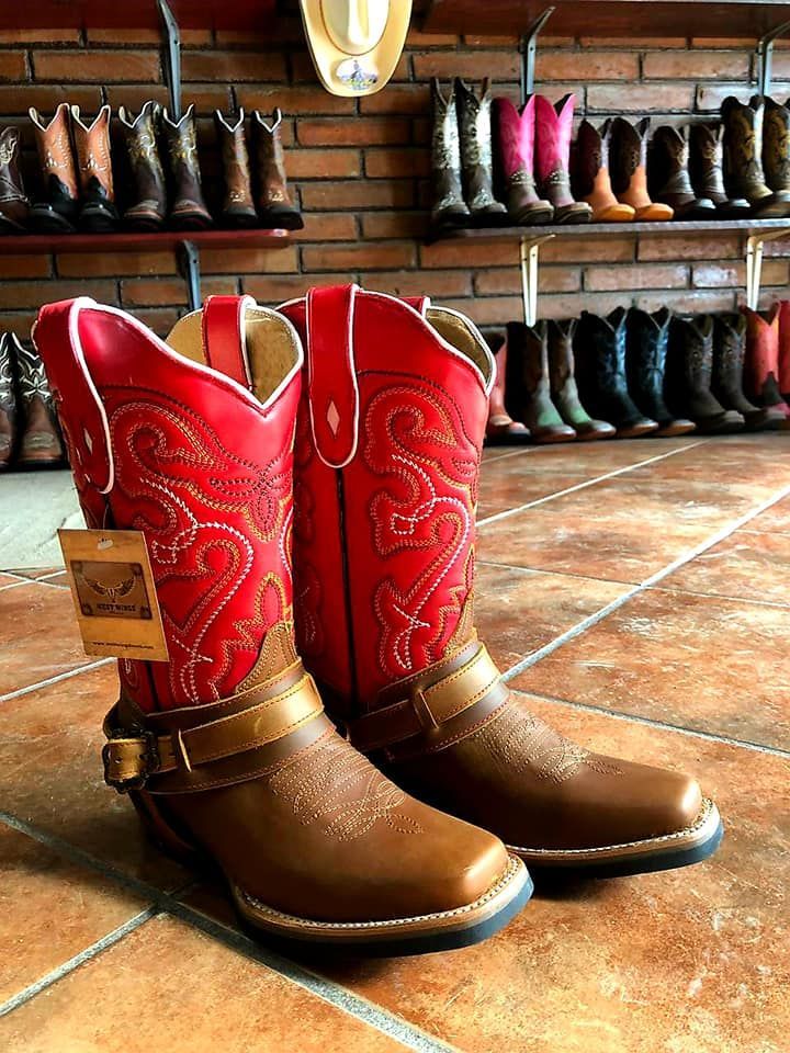 A pair of red and brown cowboy boots are sitting on a tiled floor.