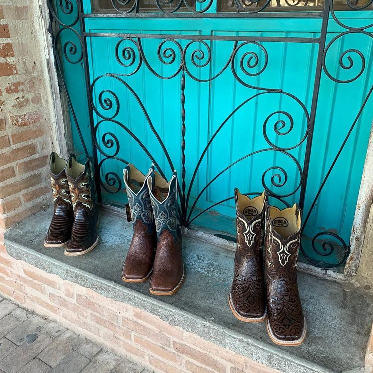 Three pairs of cowboy boots are sitting on a window sill in front of a blue door.