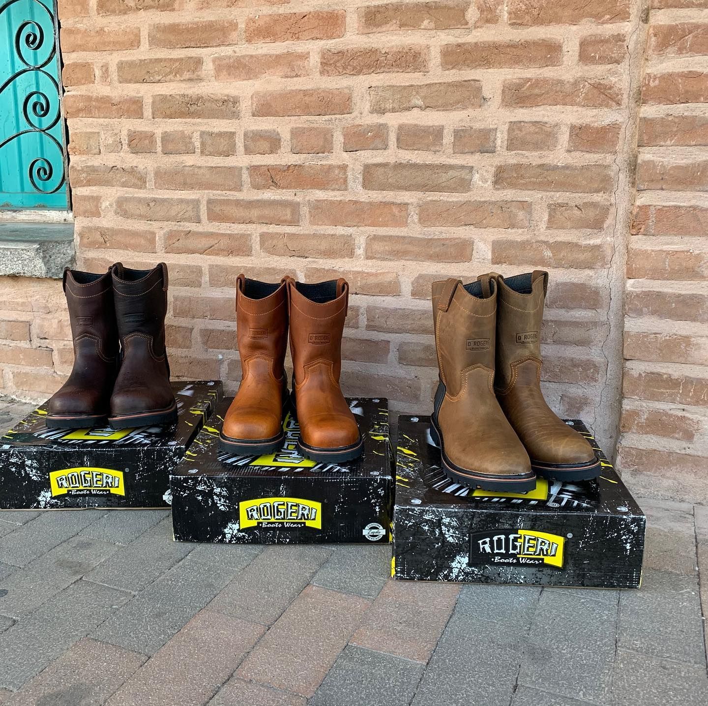 A row of cowboy boots are lined up in front of a brick wall