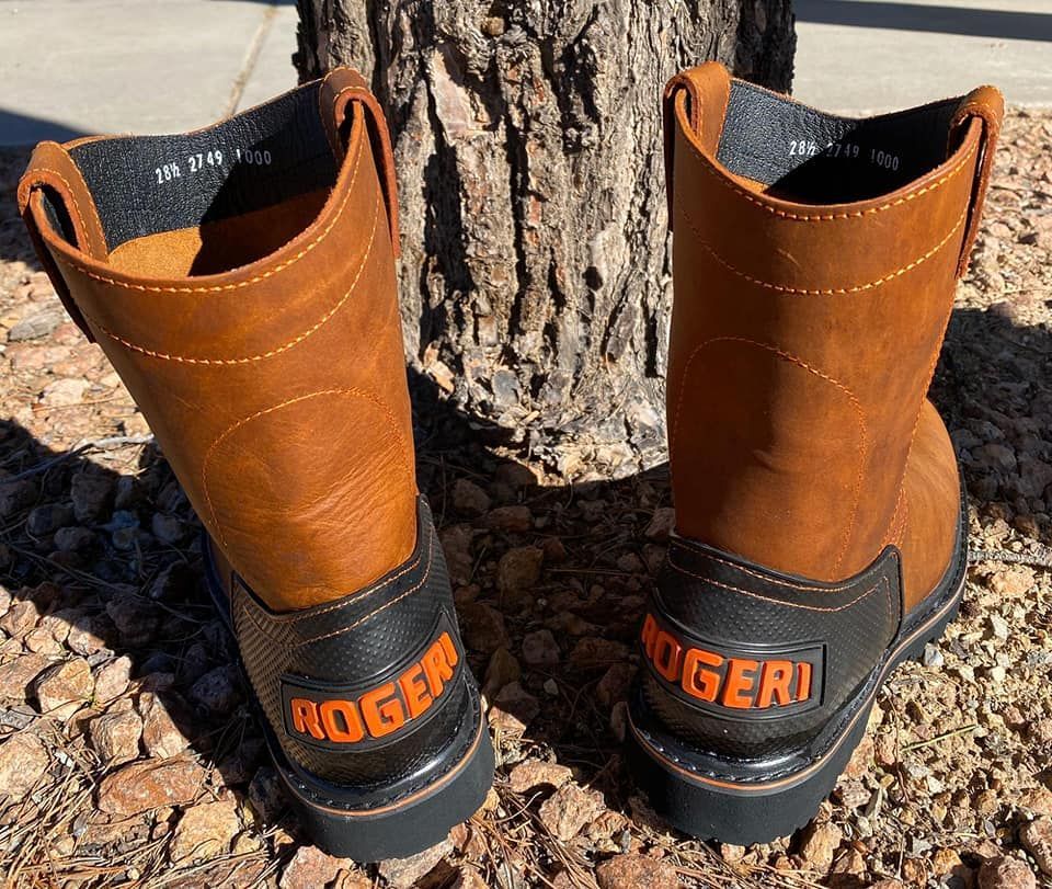 A pair of brown and black roger boots are sitting next to a tree.