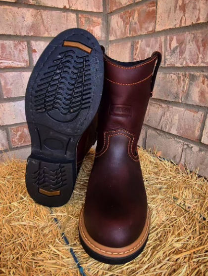 A pair of brown boots are sitting on a pile of hay in front of a brick wall.