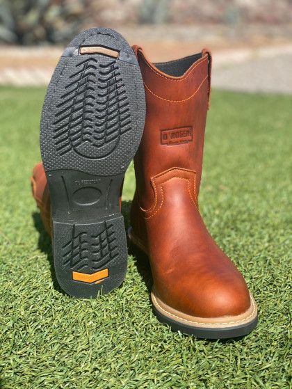 A pair of brown cowboy boots are sitting on top of a lush green field.