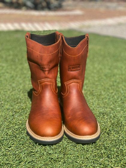 A pair of brown leather boots are sitting on top of a lush green field.