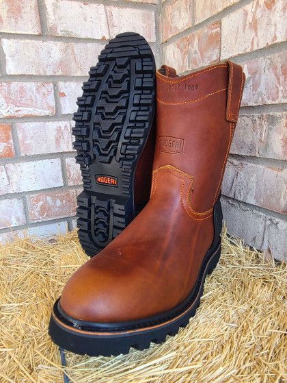 A pair of brown leather boots are sitting on a pile of hay in front of a brick wall.