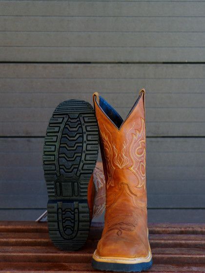 A pair of brown cowboy boots are sitting on a wooden bench.