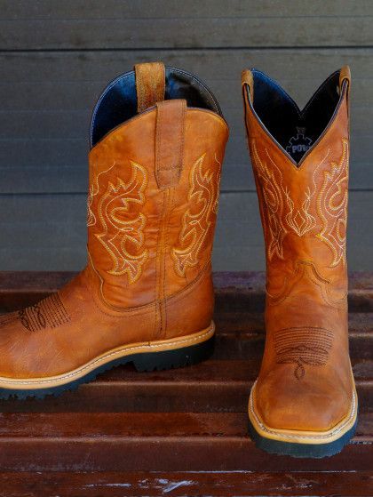 A pair of brown cowboy boots are sitting on a wooden bench.
