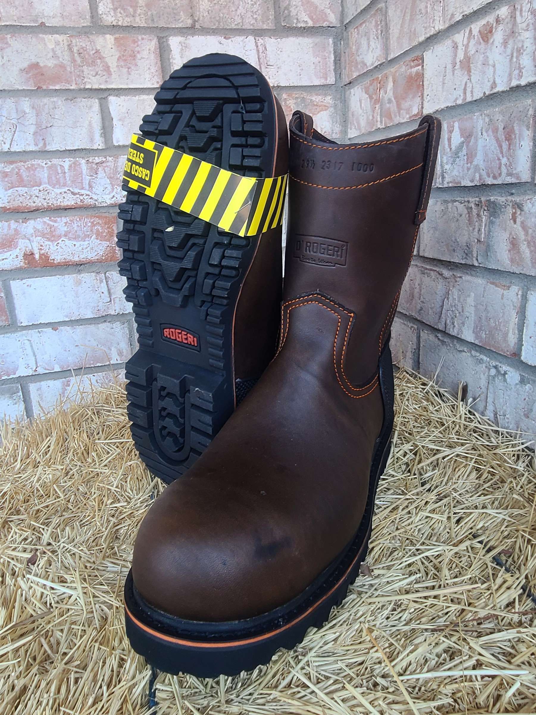A pair of brown boots are sitting on top of a pile of hay.