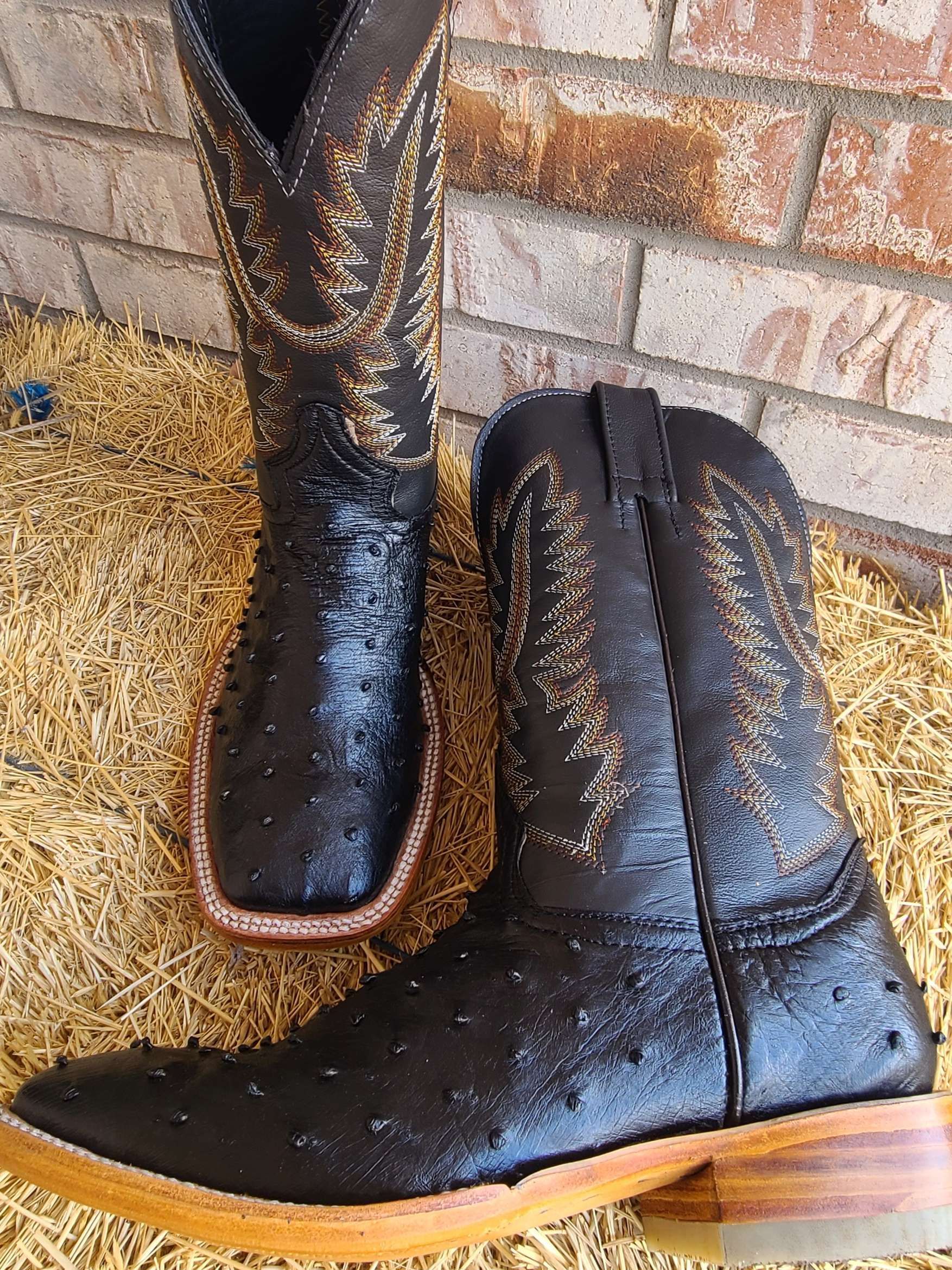A pair of black cowboy boots are sitting on a pile of hay.