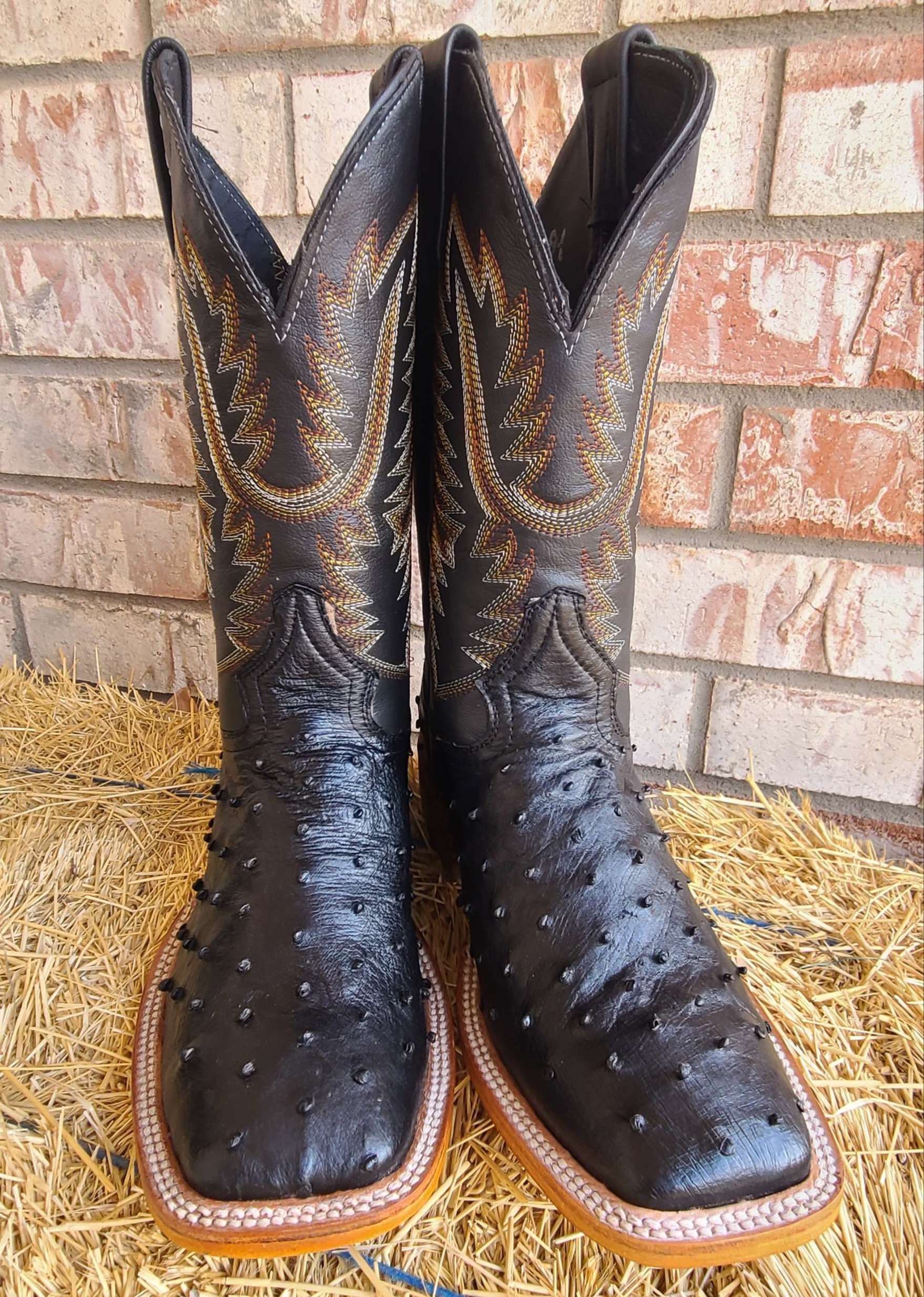 A pair of black cowboy boots are sitting on a pile of hay.
