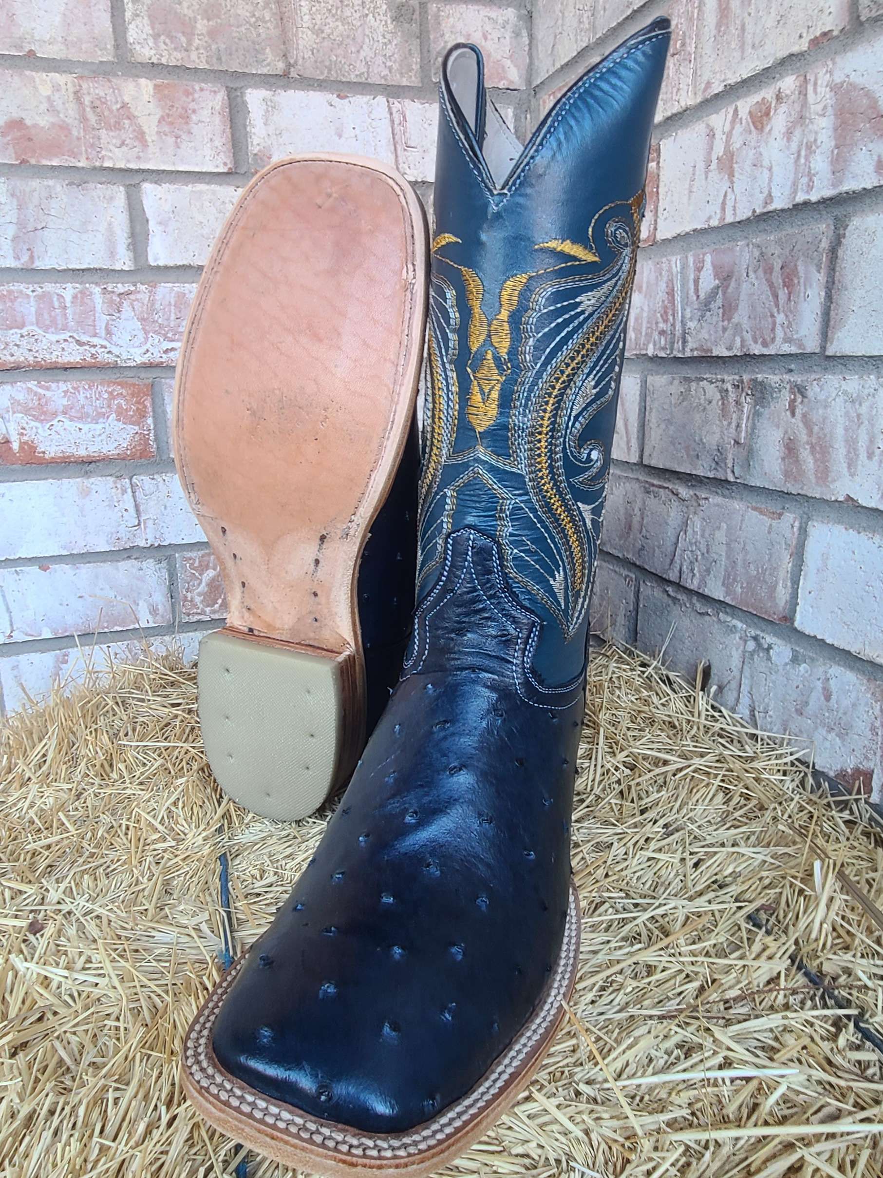 A pair of black cowboy boots are sitting on top of a pile of hay.