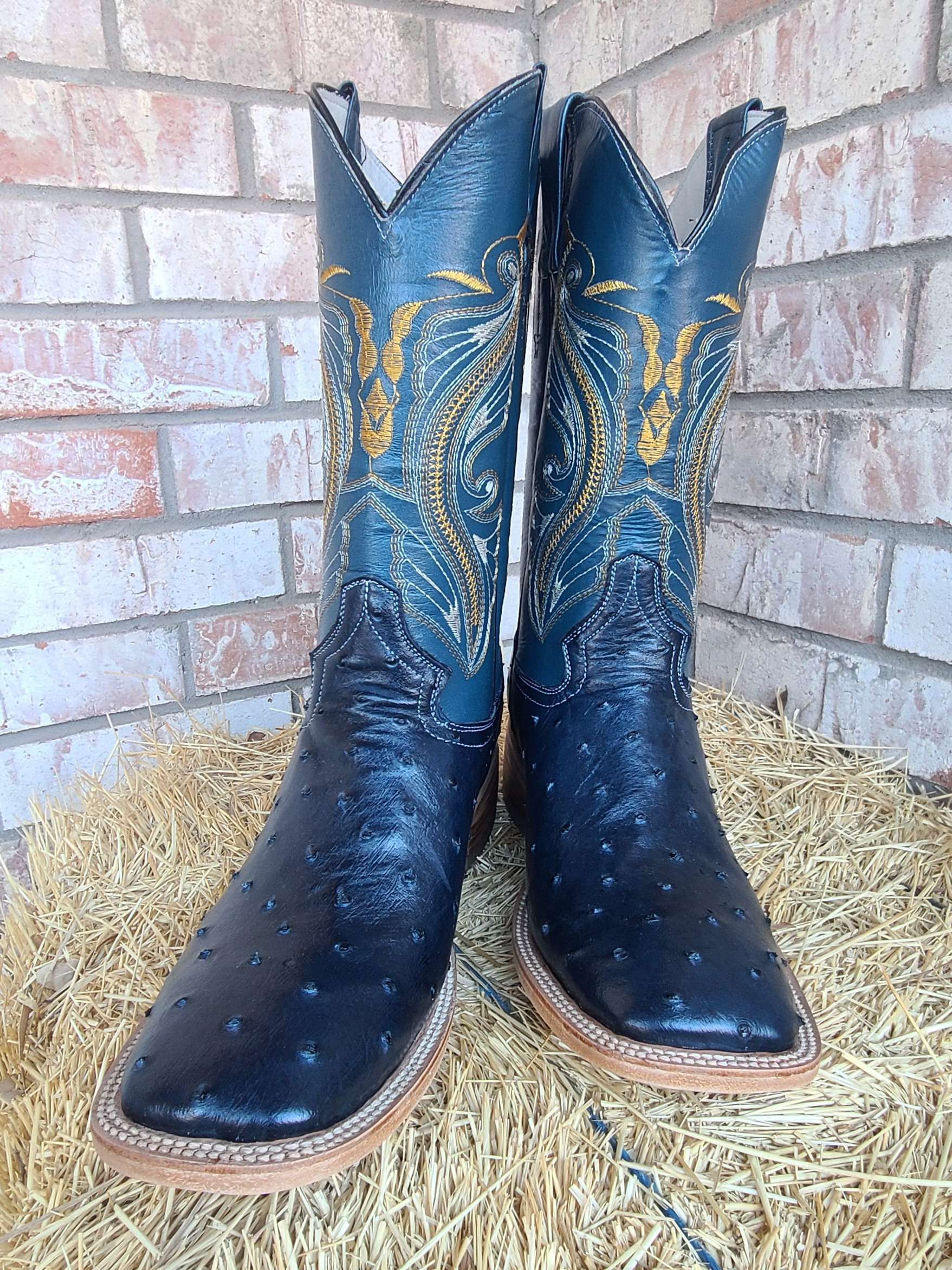 A pair of black cowboy boots are sitting on top of a pile of hay.