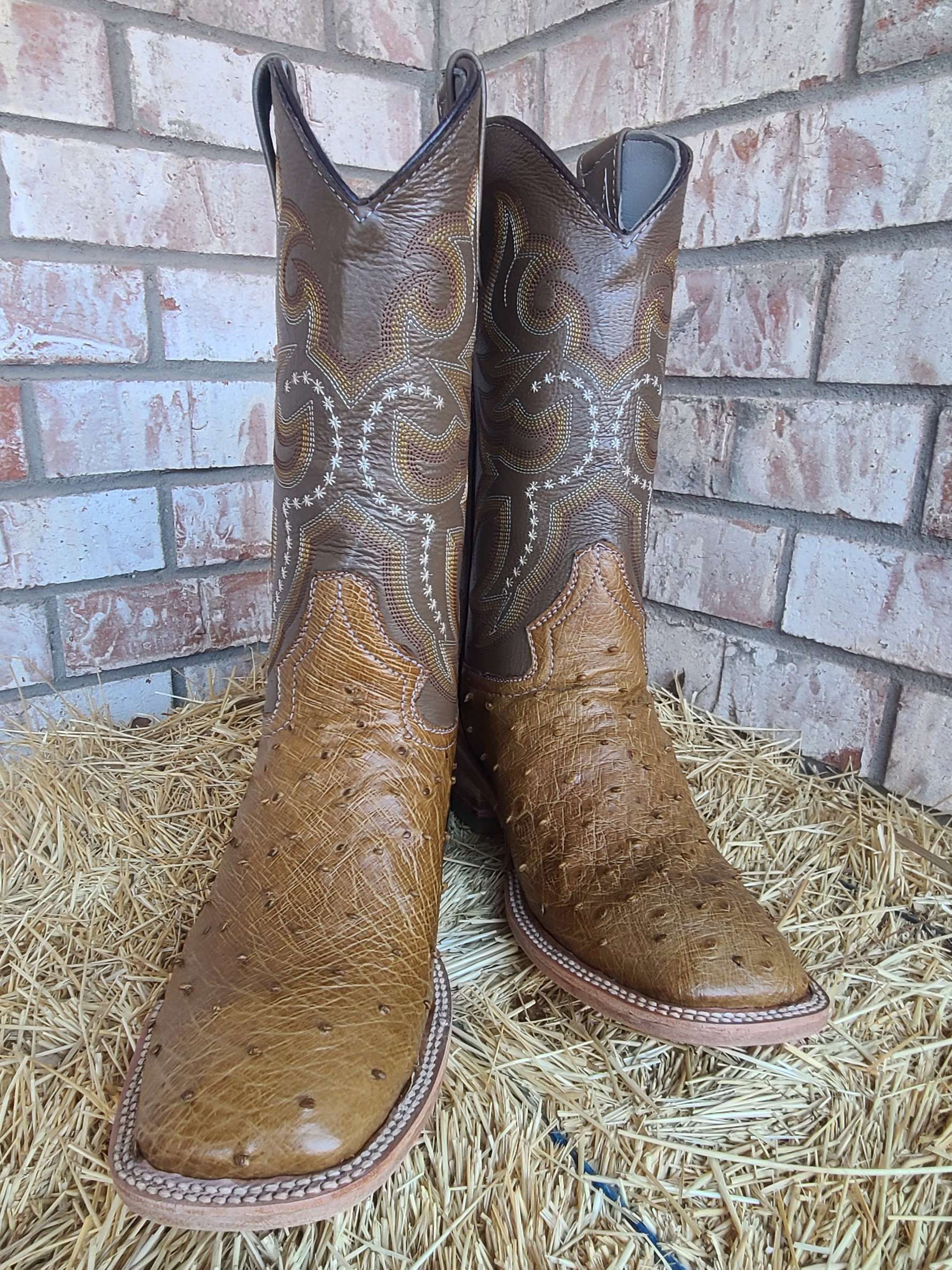 A pair of brown cowboy boots are sitting on top of a pile of hay.