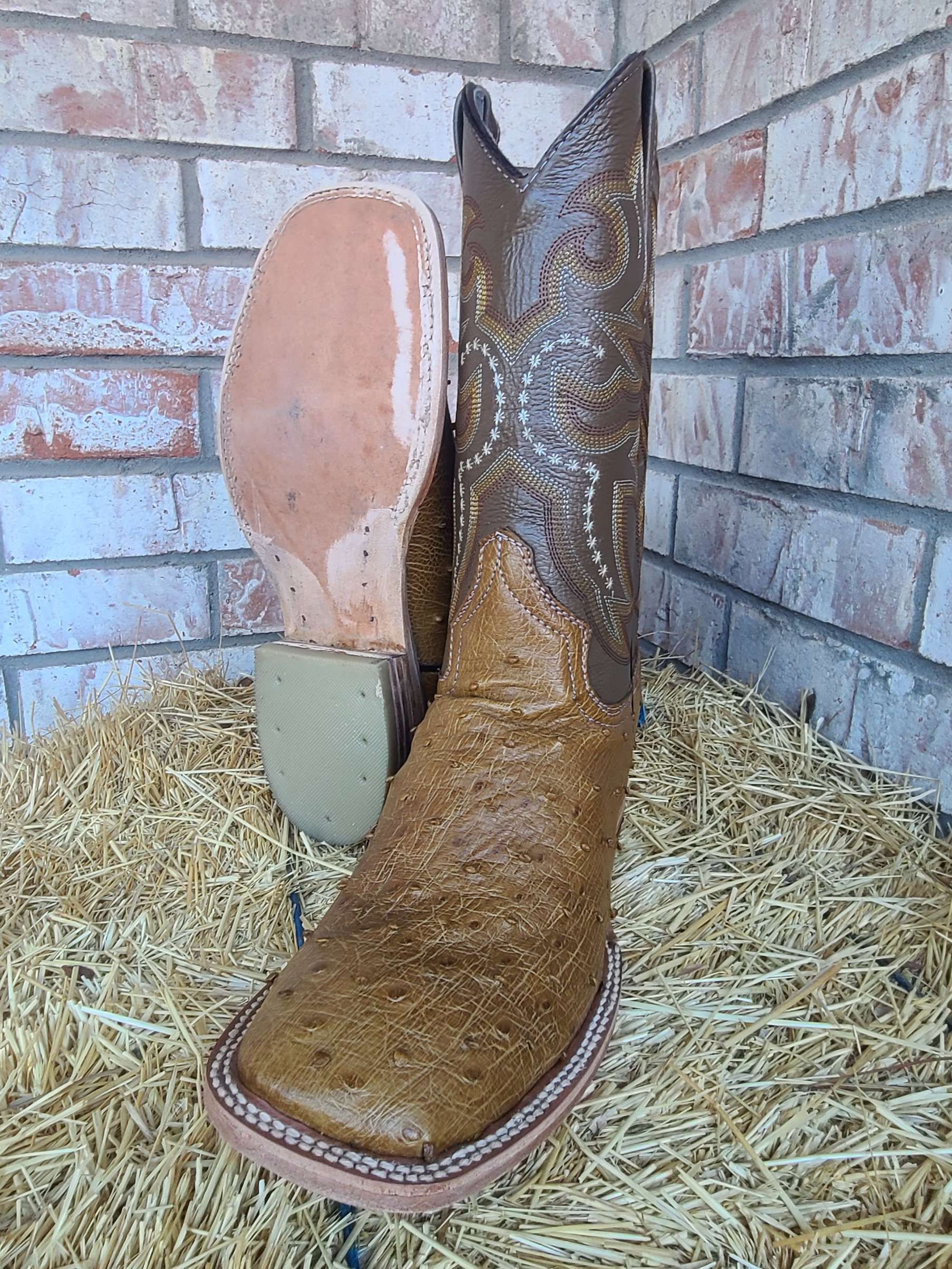 A pair of brown cowboy boots are sitting on top of a pile of hay.