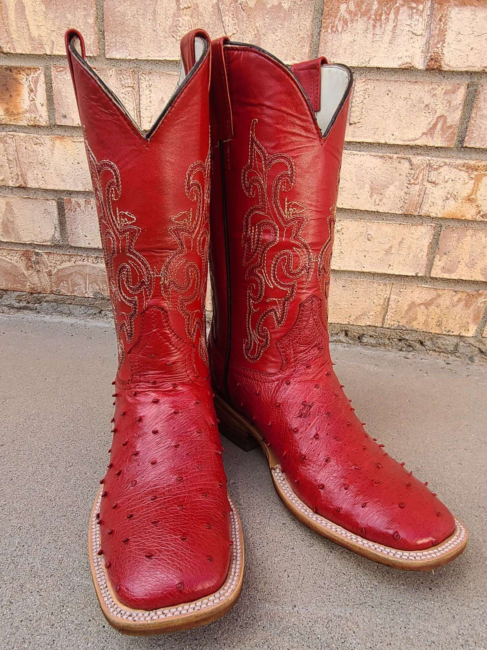 A pair of red cowboy boots are sitting on the ground in front of a brick wall.